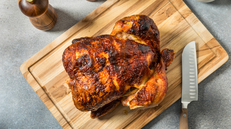 A rotisserie chicken rests on a wooden cutting board