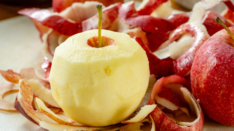A peeled apple surrounded by peelings
