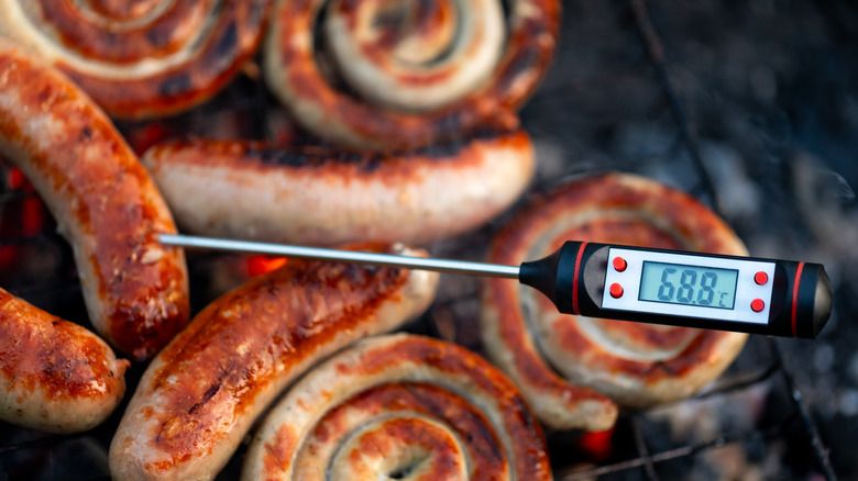 A digital meat thermometer sticks out from a group of sausages on a grill