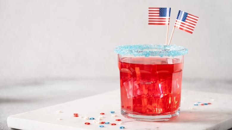 A red drink with a blue sugar rim garnished with American flag toothpicks