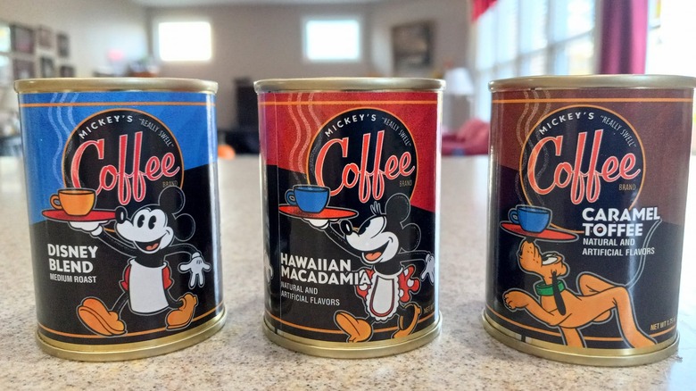 Three cans of coffee featuring Mickey Mouse and Pluto sit on a counter