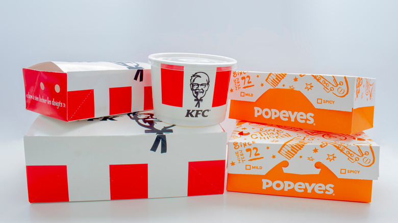 Boxes of KFC and of Popeyes sit next to each other on a white table