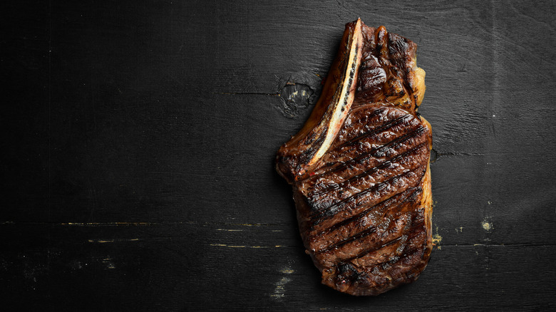 A bone-in steak, grilled to perfection, sits on a dark wooden surface