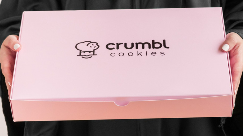 Hands holding box of Crumbl cookies