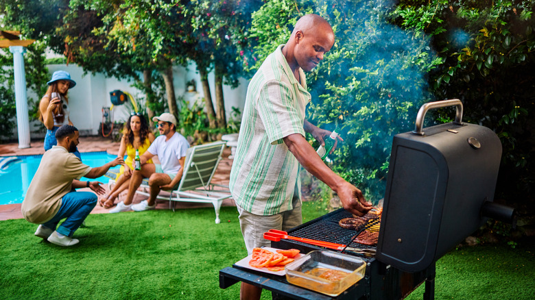 A man tends to the grill at a backyard cookout