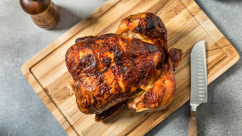 Rotisserie chicken sits on a cutting board next to a knife