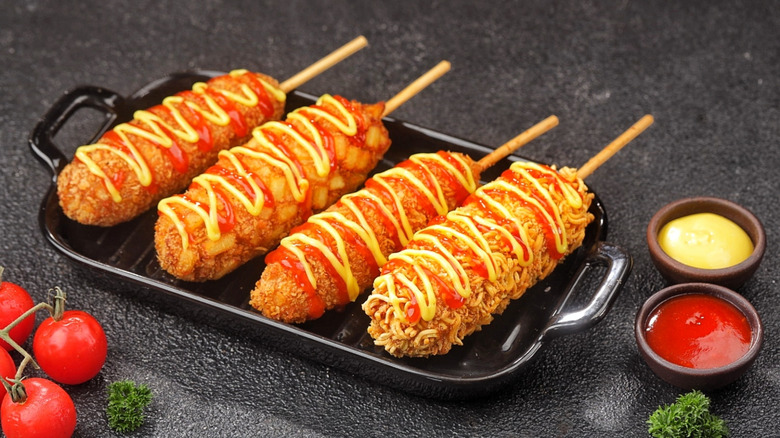 Four different styles of Korean corn dogs with ketchup and mustard.