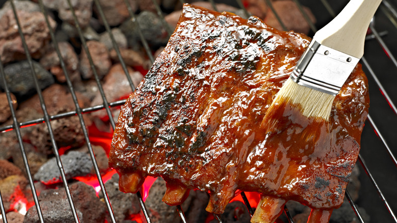 Brushing BBQ sauce onto ribs on a grill.