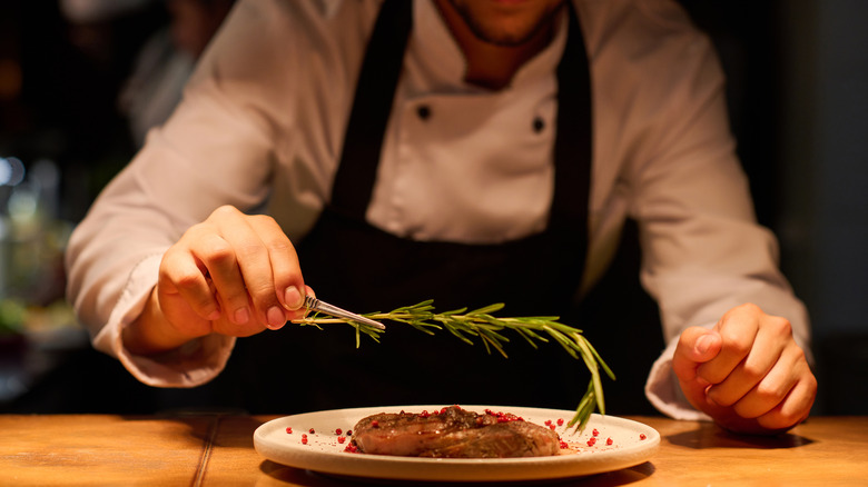 man holding rosemary sprig above steak