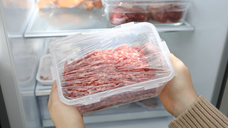 A person pulls a pack of ground beef out of the fridge