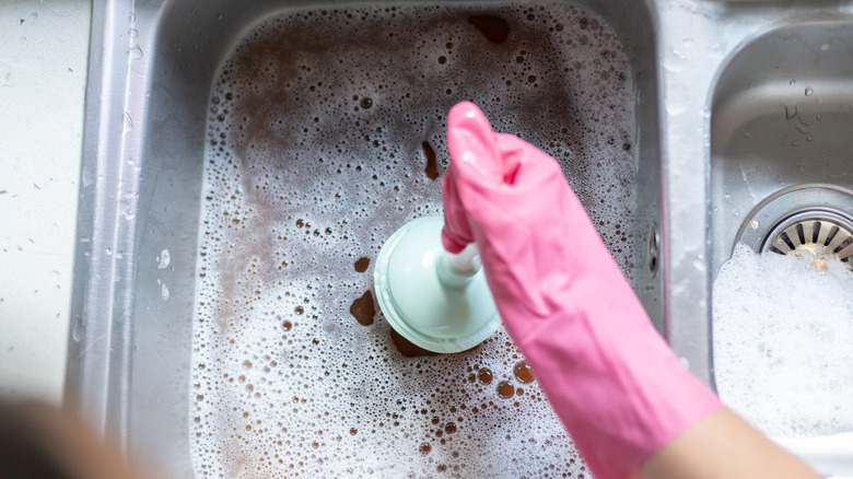 A homeowner uses a plunger on a clogged sink