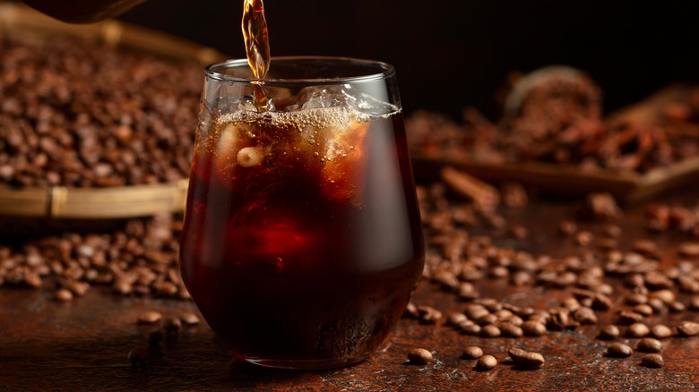 Glass tumbler of iced coffee surrounded by coffee beans