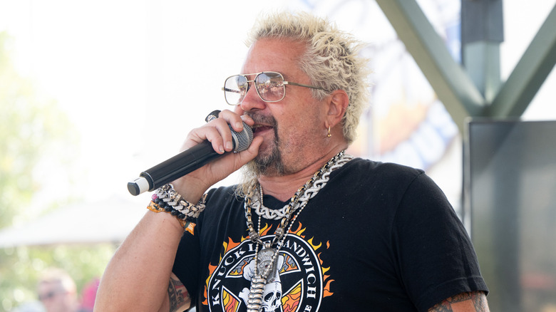 Guy Fieri holding a microphone on outdoor stage