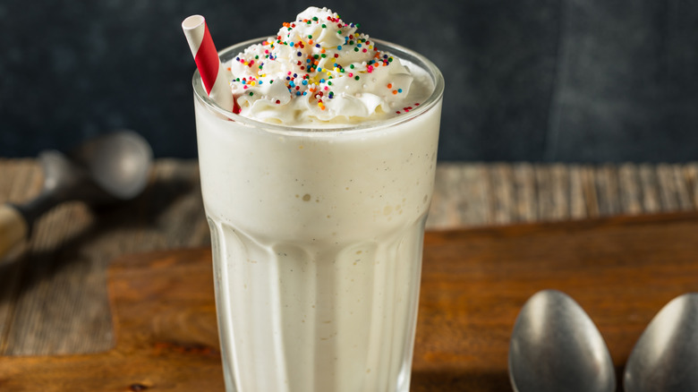 Vanilla milkshake with whipped cream and sprinkles in a tall glass with a straw