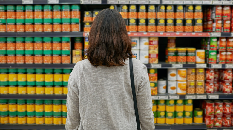 A shopper standing in front of a section of canned food in the grocery store