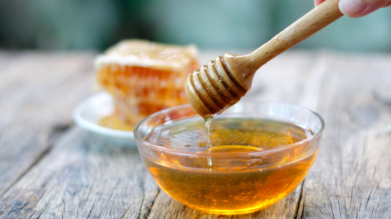 Close up bowl of honey drizzling off wooden stir stick
