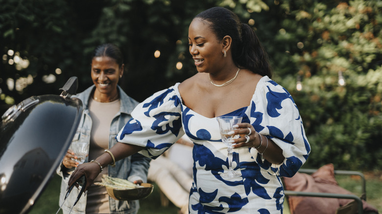 Person grilling food with a glass of wine in hand.
