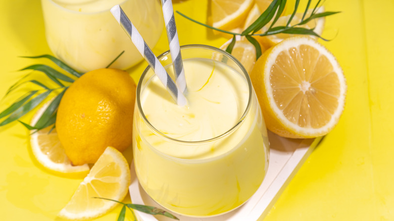 A creamy lemon drink sits in a glass with lemons around it