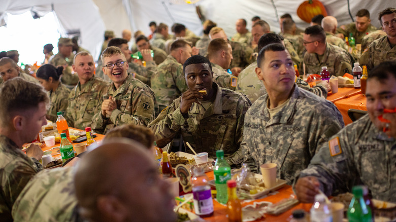 A platoon of soldiers eats at long mess tables