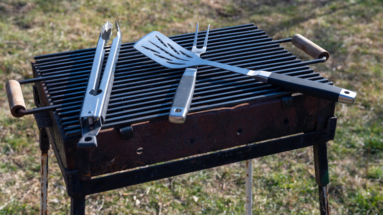 Grill utensils sit on the grates of a rectangular charcoal grill