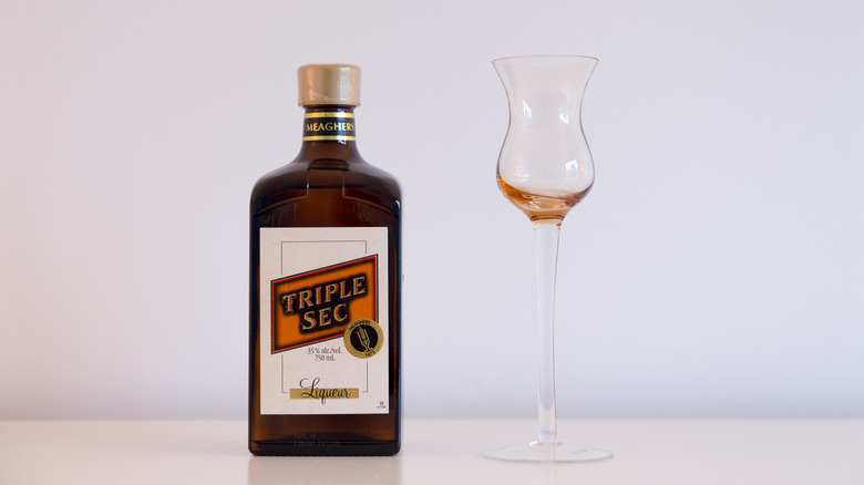 A bottle of triple sec sits next to a long sherry glass with a bit of triple sec in it