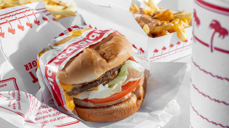 An In-N-Out cheeseburger sits in its wrapper next to animal-style fries and a drink