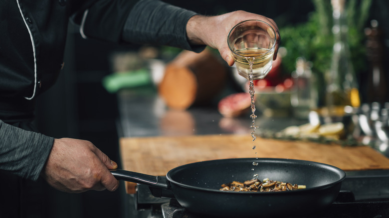 Wine being poured into a pan of mushrooms on the stove.