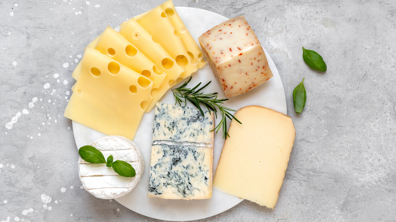 A selection of French and Italian cheeses on a platter with fresh herbs