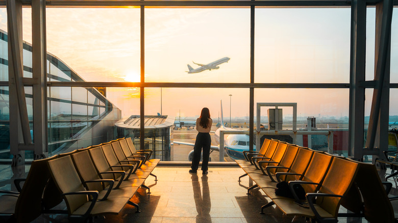 A person in an airport watching a plane take off