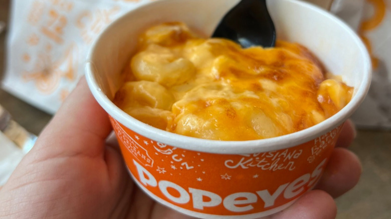 Person holding a container of Popeyes mac and cheese