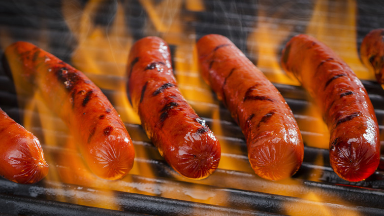 Hot dogs cooking on a flaming grill