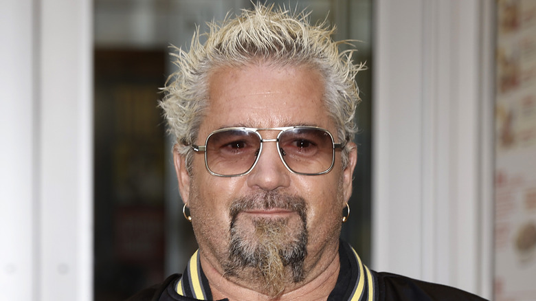 Guy Fieri excitedly smiling with sunglasses on at an event