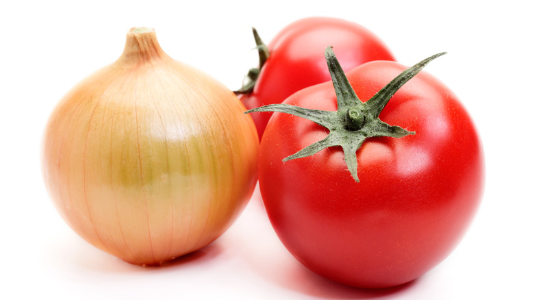 Two fresh tomatoes sit next to an unpeeled yellow onion