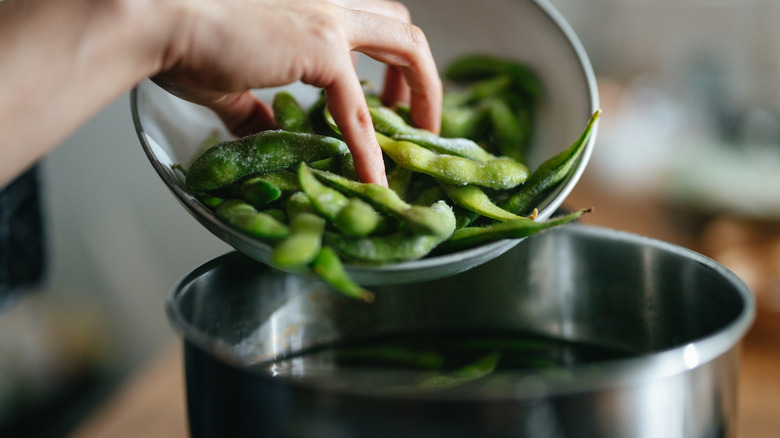 Someone adds edamame to a pot