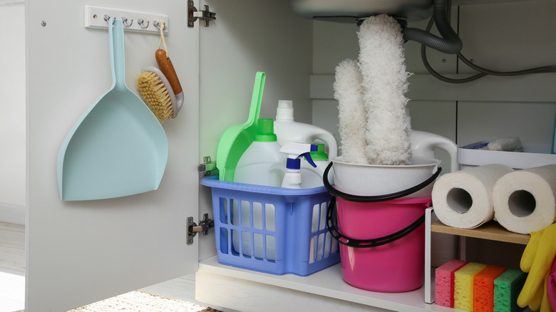 An under-sink kitchen cupboard is filled with cleaning supplies made orderly by the use of various organizational items