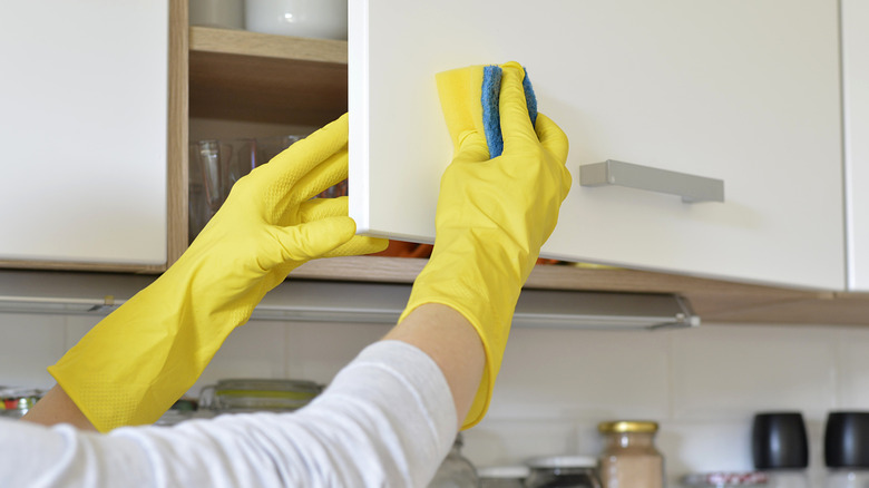 Person cleaning their kitchen cabinets with a sponge