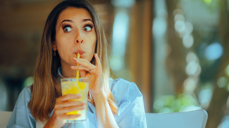 A woman drinks a glass of lemonade with a yellow striped straw