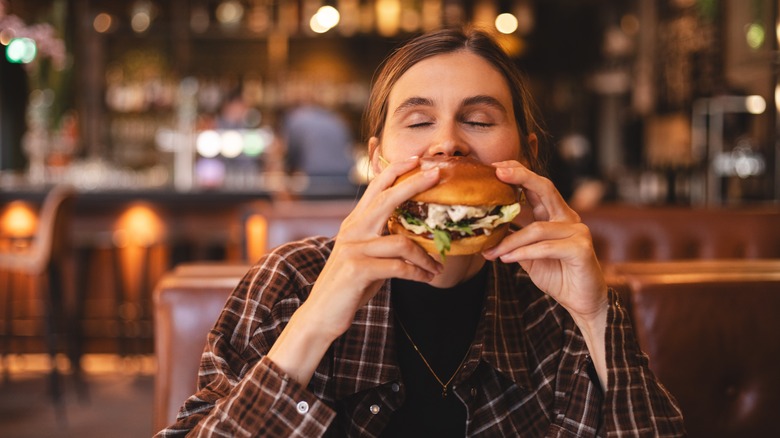 A person takes a huge bite out of a thick burger in a restaurant