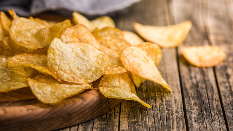 Crispy potato chips on a cutting board on a wood table