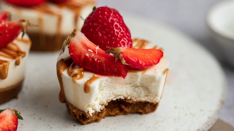 A mini cheesecake topped with strawberries, with a bite taken out of it.