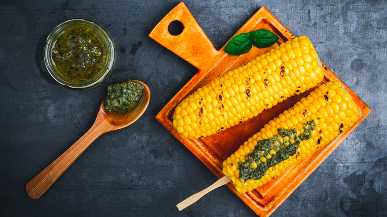 Corn on the cob that has been charred and has an herby green sauce spread on it