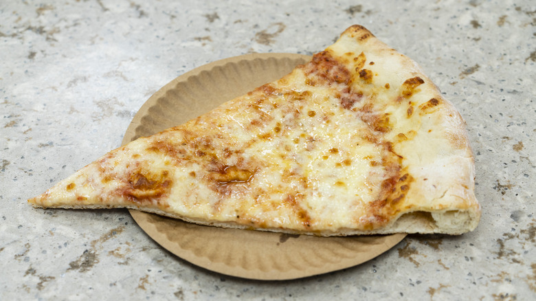 A plain slice of NYC pizza sits on a brown paper plate