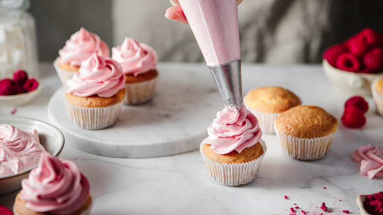 Person piping pink frosting on cupcakes