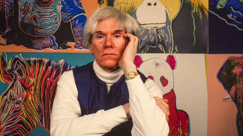 Andy Warhol posing in front of paintings