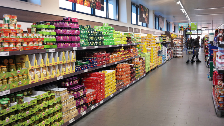 A redhaired woman holds a bottle of sauce in a supermarket aisle