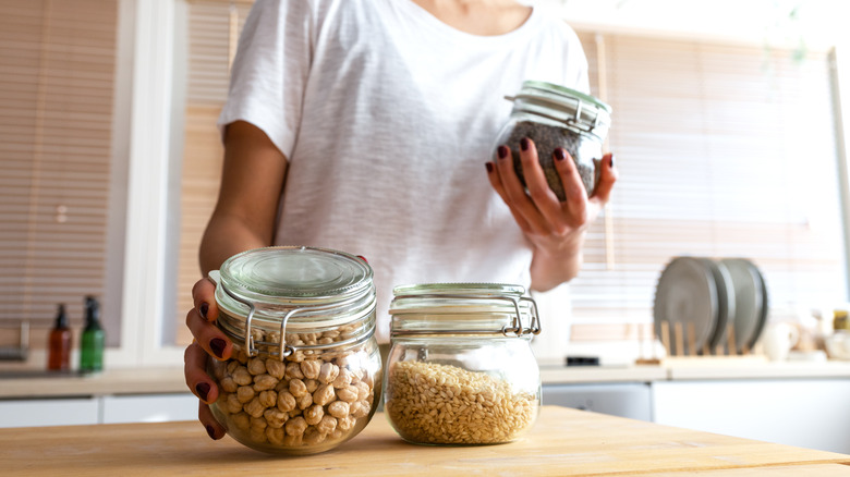A woman holding a few jars of dry goods in a kitchen