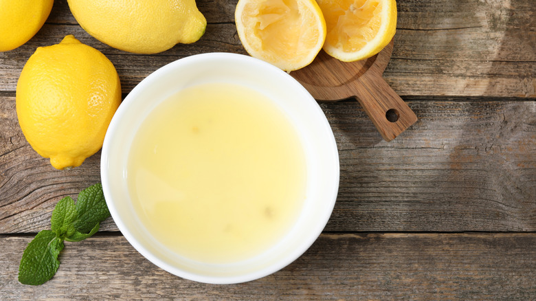 Fresh lemon juice in bowl by halved lemon and full lemons