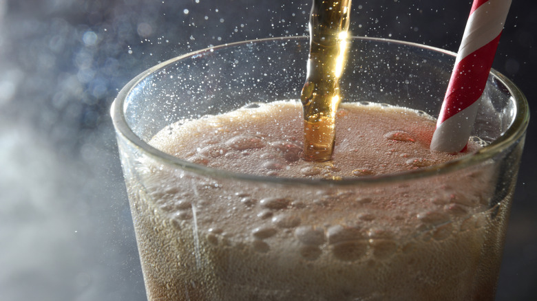 Closeup of soda being poured into a glass cup with a red-and-white straw in it
