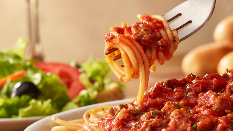 Spaghetti with meat sauce on a white plate and being twirled on a fork