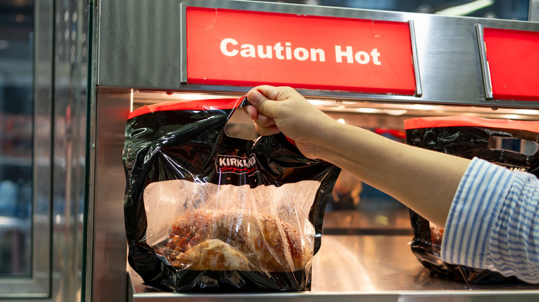 A woman's hand holds a bagged Costco rotisserie chicken